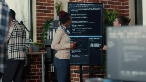 Programmer Holding Digital Tablet Analyzing Code on Wall Screen Tv While Colleague is Looking for