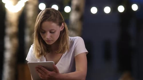 Bbeautiful Young Girl Working on a Tablet in the Evening