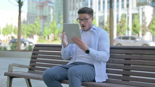 Man On Bench Using Tablet with Surprised Expression