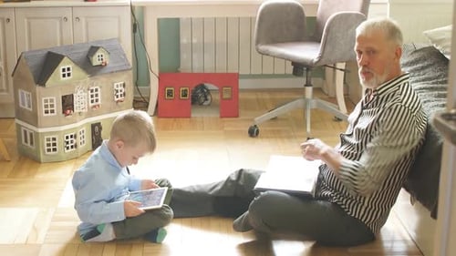 Grandfather and Grandson Reading on Floor Indoors