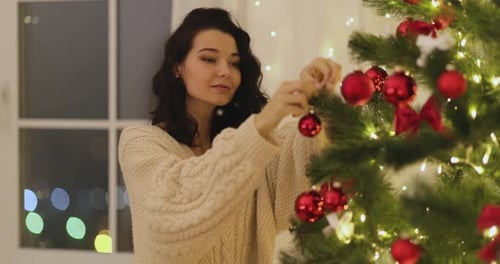 Woman Decorates Christmas Tree with Red Ornaments