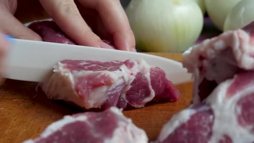 Hands slicing raw meat on cutting board