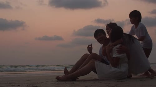 Dad, mom and kid sit, hug relax together near sea when looking silhouette sunset.