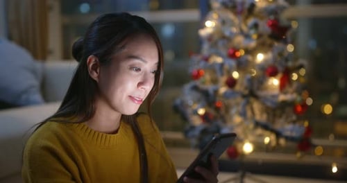 Woman Using Phone at Home Near Christmas Tree