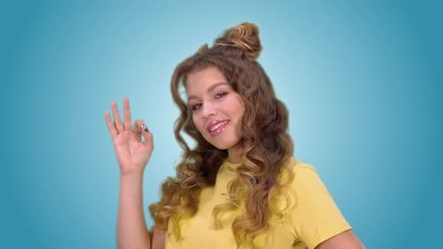 Smiling Woman Gives Okay Sign on Blue, Green Background