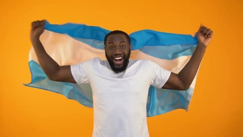 Man Celebrates with Flag in Front of Orange Background