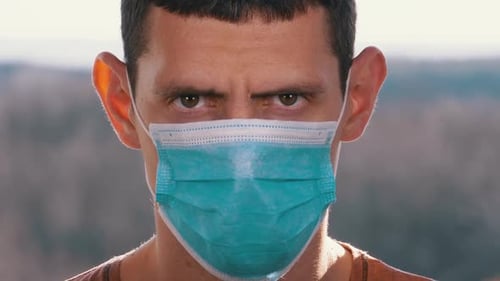 Young Man in a Medical Protective Face Mask Looking at the Camera on the Street Background