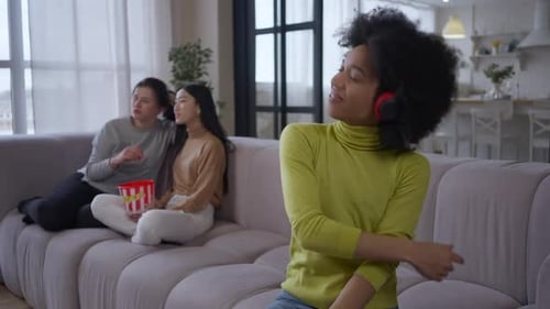 Heureuse femme afro-américaine joyeuse appréciant de la musique dans des écouteurs dansant assise sur le canapé avec