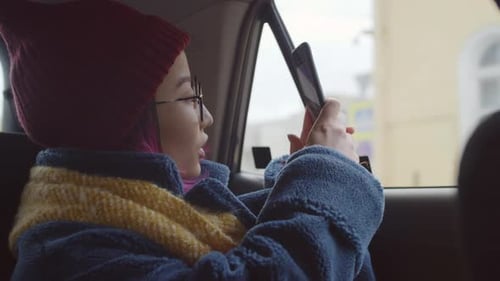 Cheerful Asian Female Tourist Riding in Car and Taking Photo with Phone