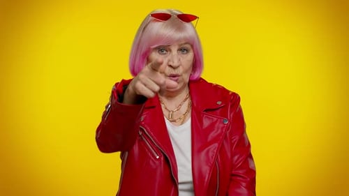 Ältere alte Frau zeigt mit verspieltem, fröhlichem Ausdruck auf die Kamera und zeigt die Richtung