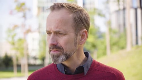 A Middleaged Handsome Caucasian Man Smiles at the Camera in a Park in an Urban Area Closeup