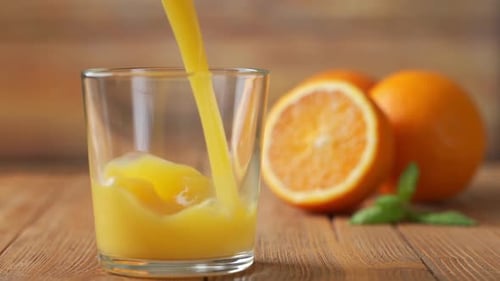 Pouring Orange Juice in Glass on Wooden Table
