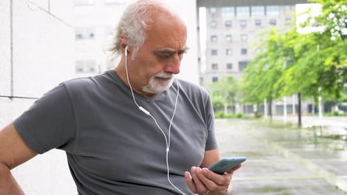 Senior Man Using Smartphone with Headphones Outdoors