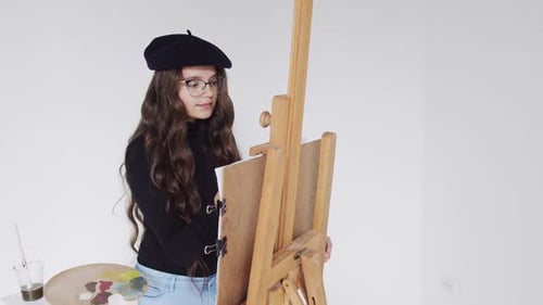 Young Woman Artist in Beret Painting Picture on Canvas in Art Studio