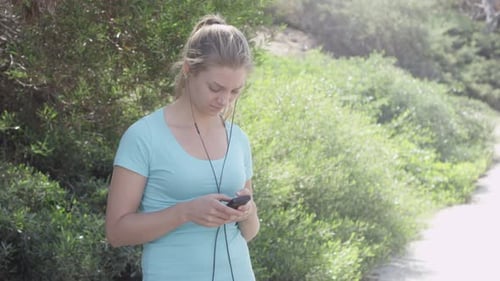 A young woman runner putting on earbuds before going on a run.