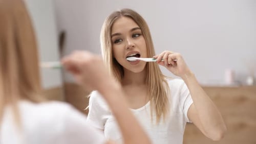 Young Woman Brushing Teeth in Bathroom Mirror