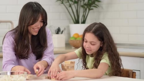 Joyful Mother and Cheerful Daughter Play a Board Game at Home at the Table Building a Tower of