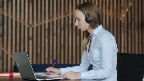Woman Using Laptop and Headset in Office