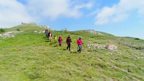 Group Hiking Up Green Mountain Hillside on Sunny Day
