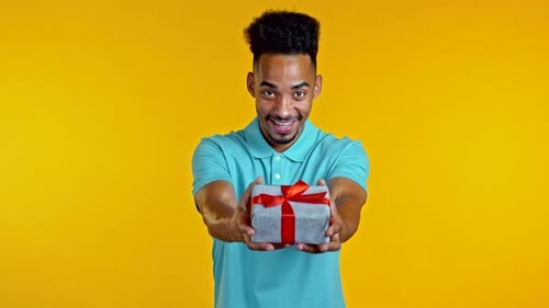 Man Holds Out Birthday Gift on Yellow Background
