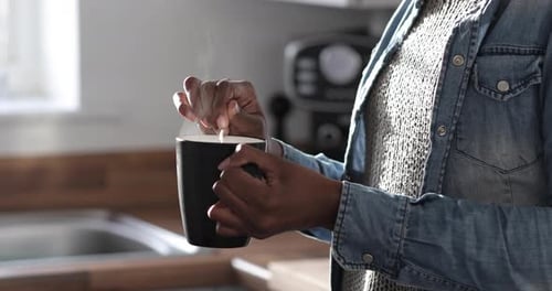 Young woman standing in kitchen, stirring hot drink, close-up