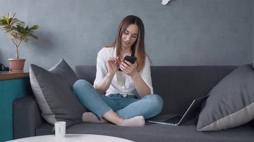 Woman Smiling Using Phone Sitting on Couch at Home