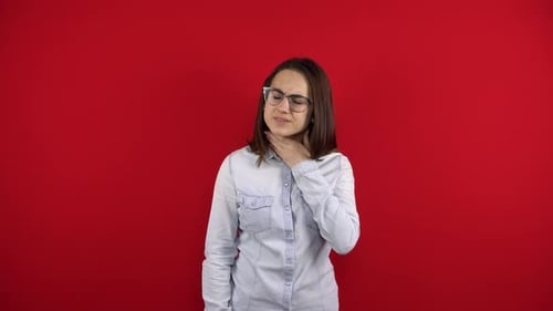 Eine junge Frau mit Brille hat Halsschmerzen und berührt ihn mit ihrer Hand