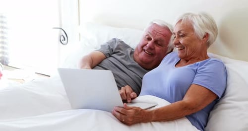 Smiling Senior Couple Using Laptop in Bed