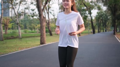 Asian sport woman is running in place double time in green park and also listen music in park