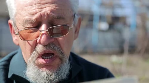 gray-haired pensioner with a mustache sitting in the garden and reading a newspaper
