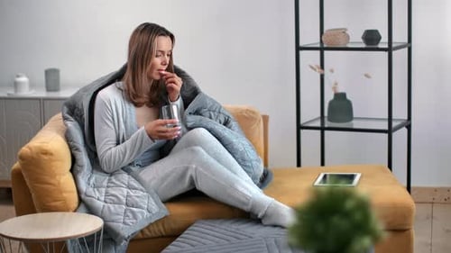 Woman Takes Pill and Drinks Water on Couch