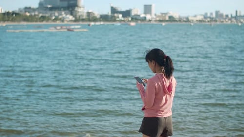 Woman Using Phone on Beach, City Background