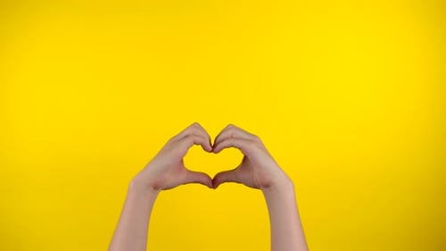 Hands Forming a Heart on Yellow Background