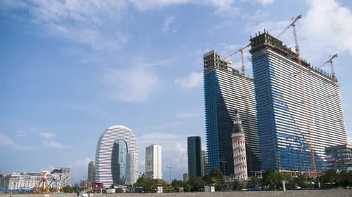 Bau eines modernen Wolkenkratzers mit Turmdrehkranen. Zeitraffer. Bewegte Wolken am blauen Himmel