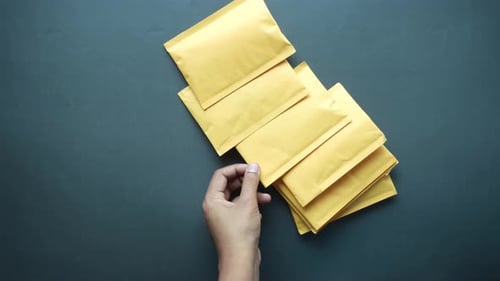 Hand Places Tan Envelope with Pile on Background