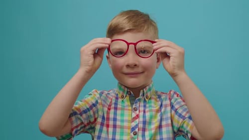 Portrait d'un garçon d'âge préscolaire souriant portant des lunettes regardant la caméra debout sur fond bleu