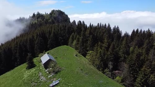 Drone Shot d'un passage de montagne avec une petite maison, une forêt et un lit de nuages
