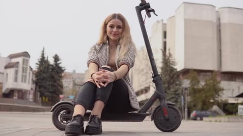 Woman Sits on Electric Scooter in Urban Setting