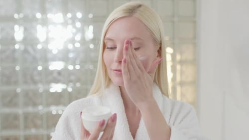 Woman Applies Face Cream in Bathroom