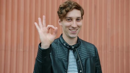 Young Adult Gives Okay Hand Gesture and Wink
