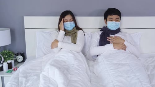 Couple Sick in Bed Wearing Masks and Scarves