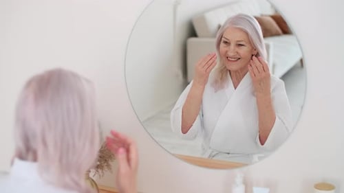 Smiling Senior Woman Massaging Her Face in Mirror
