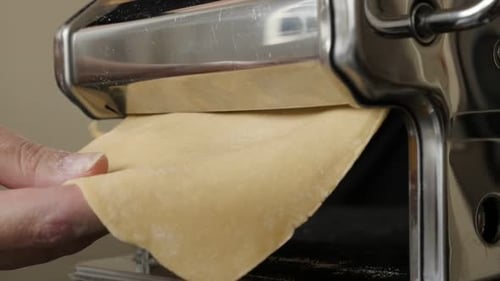 Hand feeding dough through pasta machine close up