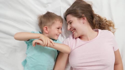 Top View Portrait of Cute Little Boy Lying with Young Mother on Bed and Talking