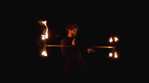Fire show artist guy twists a fire pole around his body under a bridge. Slow motion