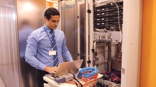 Man Works in Server Room on Laptop