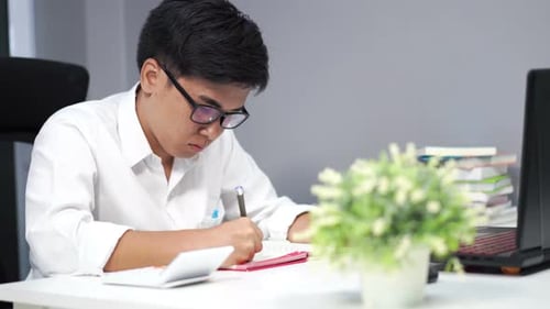 young man studying and writing on notebook with laptop computer