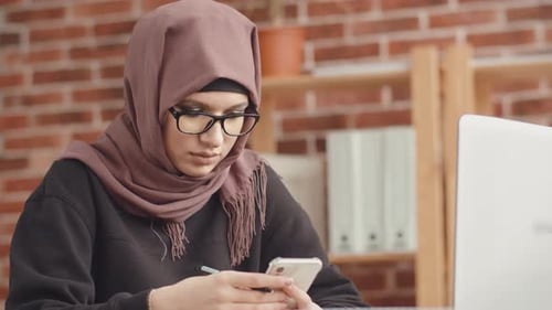 Une femme musulmane avec des lunettes tape sur son smartphone. Une fille en hijab compose un message sur elle