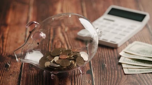 A Hand Inserting Coins in Piggybank Over Wooden Desk