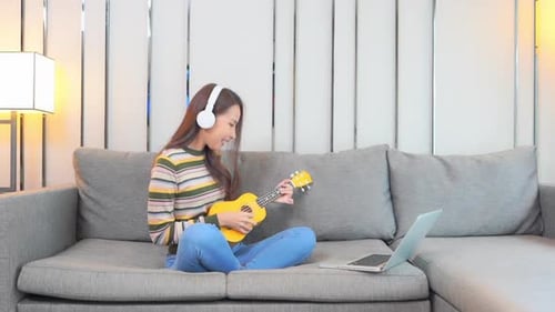 Woman Playing Ukulele at Home Wearing Headphones